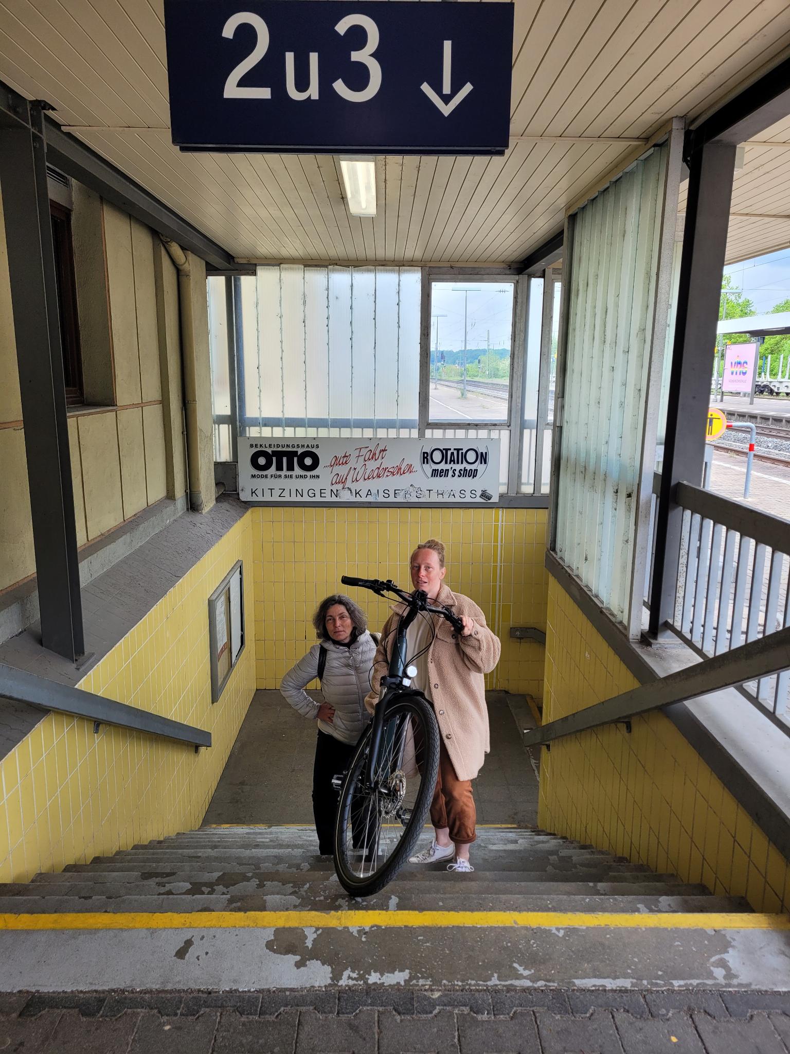 MdL Kerstin Celina und Eva-Maria Stöcklein tragen ein Fahrrad die Bahnhofstreppen hinauf.